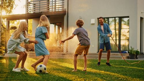 family playing in the backyard at sunset with soccer ball and hose