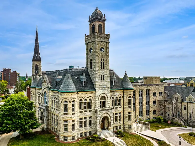 Historic stone building with clock tower and spire under a blue sky.