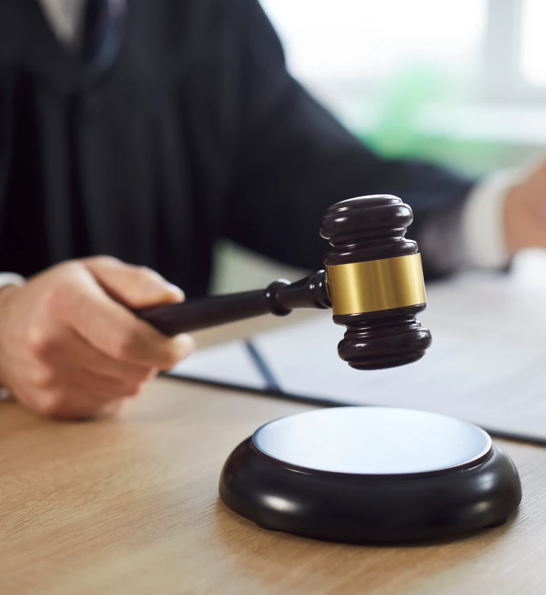 Close-up of a judge's hand holding a wooden gavel above a sound block on a desk.
