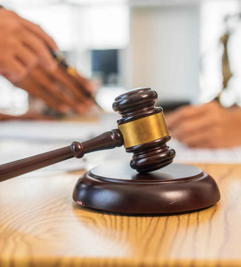 Wooden judge's gavel with brass band resting on sound block, blurred background of person writing.