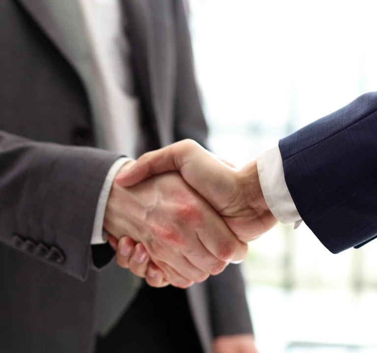Two individuals in business suits shaking hands in a professional setting.