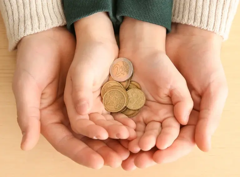 Two pairs of hands, one adult and one child, holding euro coins together.
