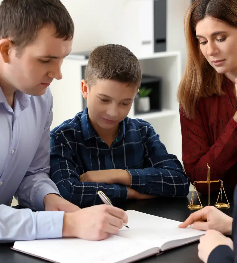 Three individuals, including a child, reviewing documents at a table with a small golden scales of justice statue.