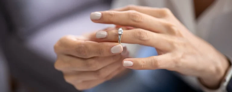 Close-up of hands placing a diamond engagement ring on a finger with neutral nail polish.