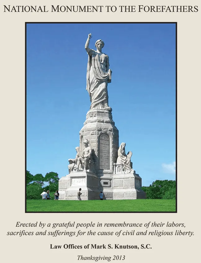 Statue of the National Monument to the Forefathers with seated figures on a grassy field.