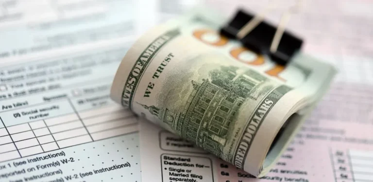 Rolled US one hundred dollar bill clipped on tax forms and financial documents.