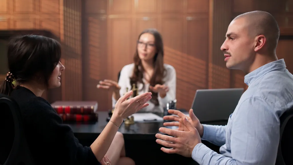 Three professionals engaged in a discussion around a table with a laptop and legal books.