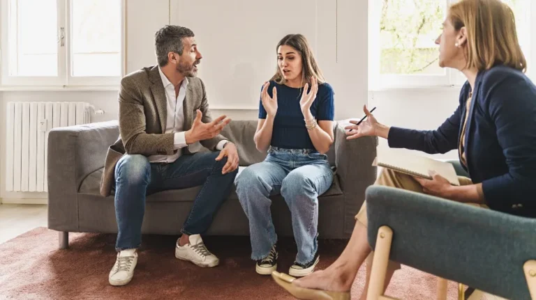Three adults engaged in a serious discussion in a bright room with natural light.
