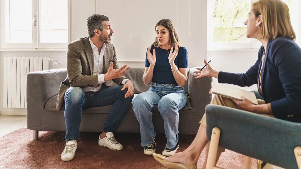 Three adults engaged in a serious discussion in a bright room with natural light.